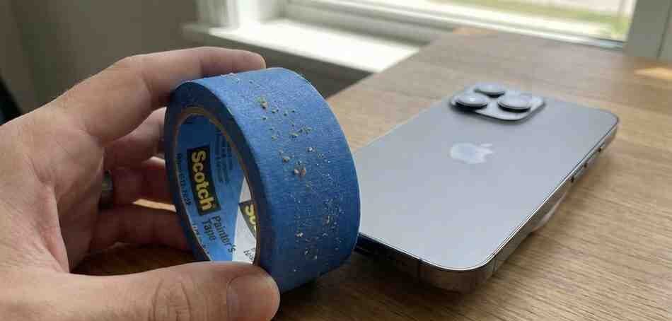 A strip of blue painter's tape rolled into a cylinder being pressed against the bottom speaker of an iPhone